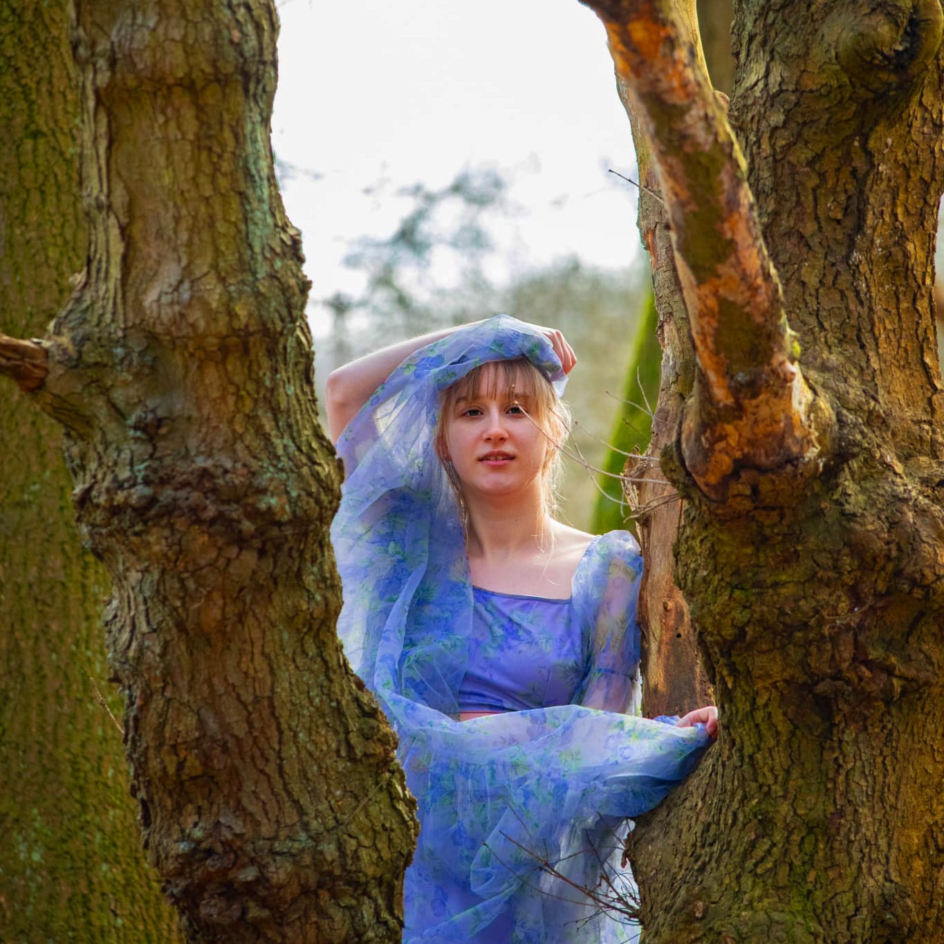 EMRY standing between the trees in the woods wearing a fairy tulle dress.